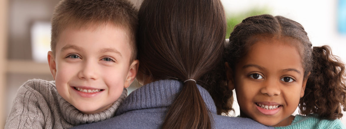 Happy children with mother Twi adoptive children of different ethnicity hugging their adoptive mother.
