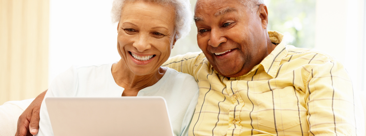 Two senior adults smiling as they using a laptop together.